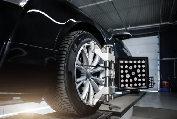 A wheel alignment target board clamped to the alloy wheel of a black car on an alignment rack in a repair shop.