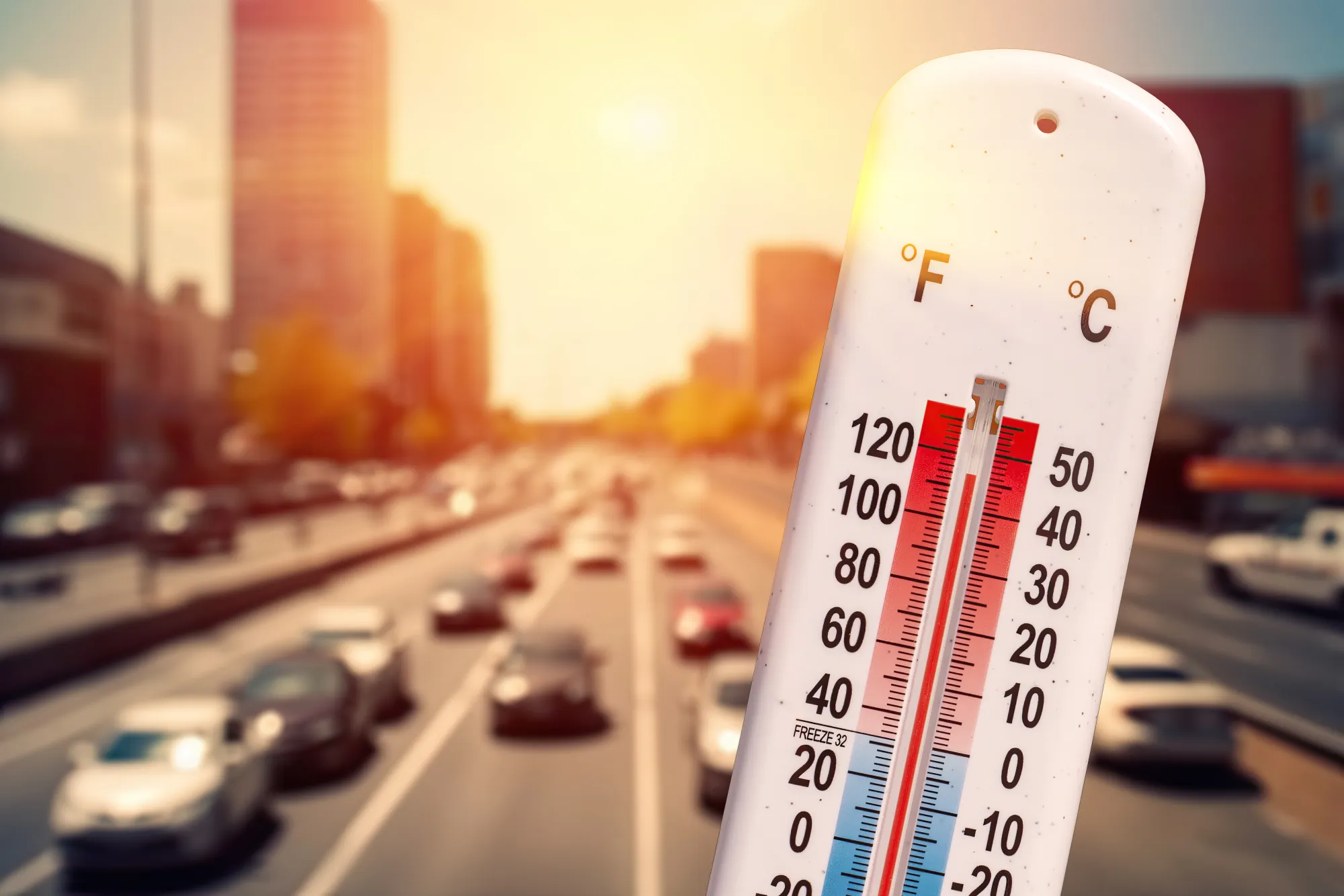 A thermometer showing over 100 degrees Fahrenheit in front of a sunlit highway full of cars.